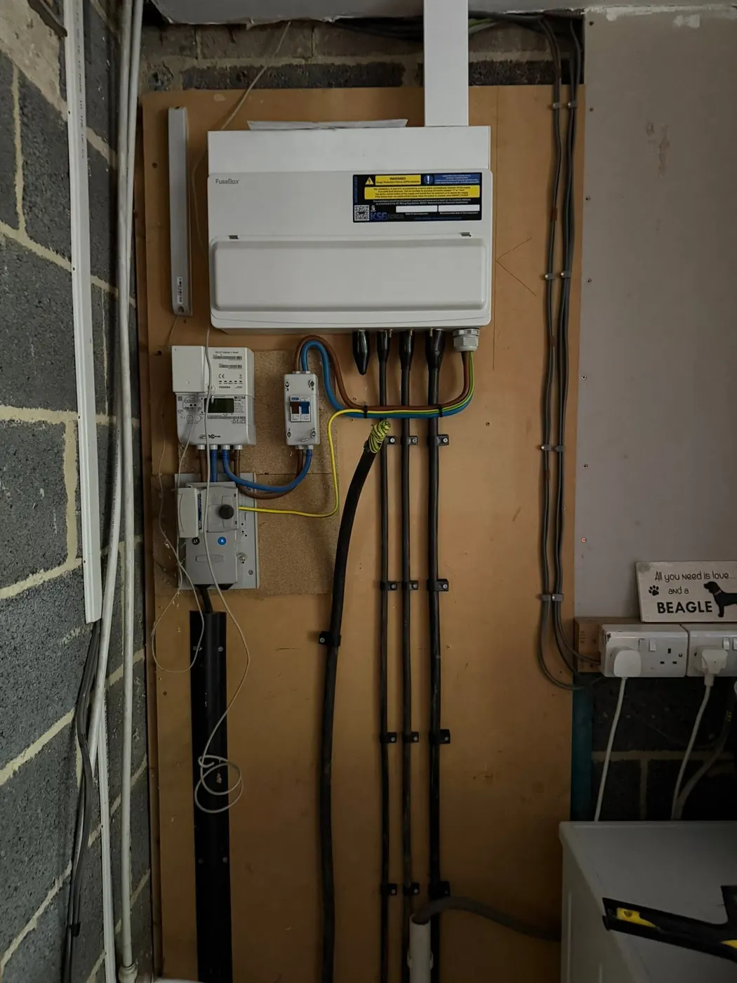 Newly installed consumer unit above a smart meter, with tails and circuit cables neatly clipped to a backboard